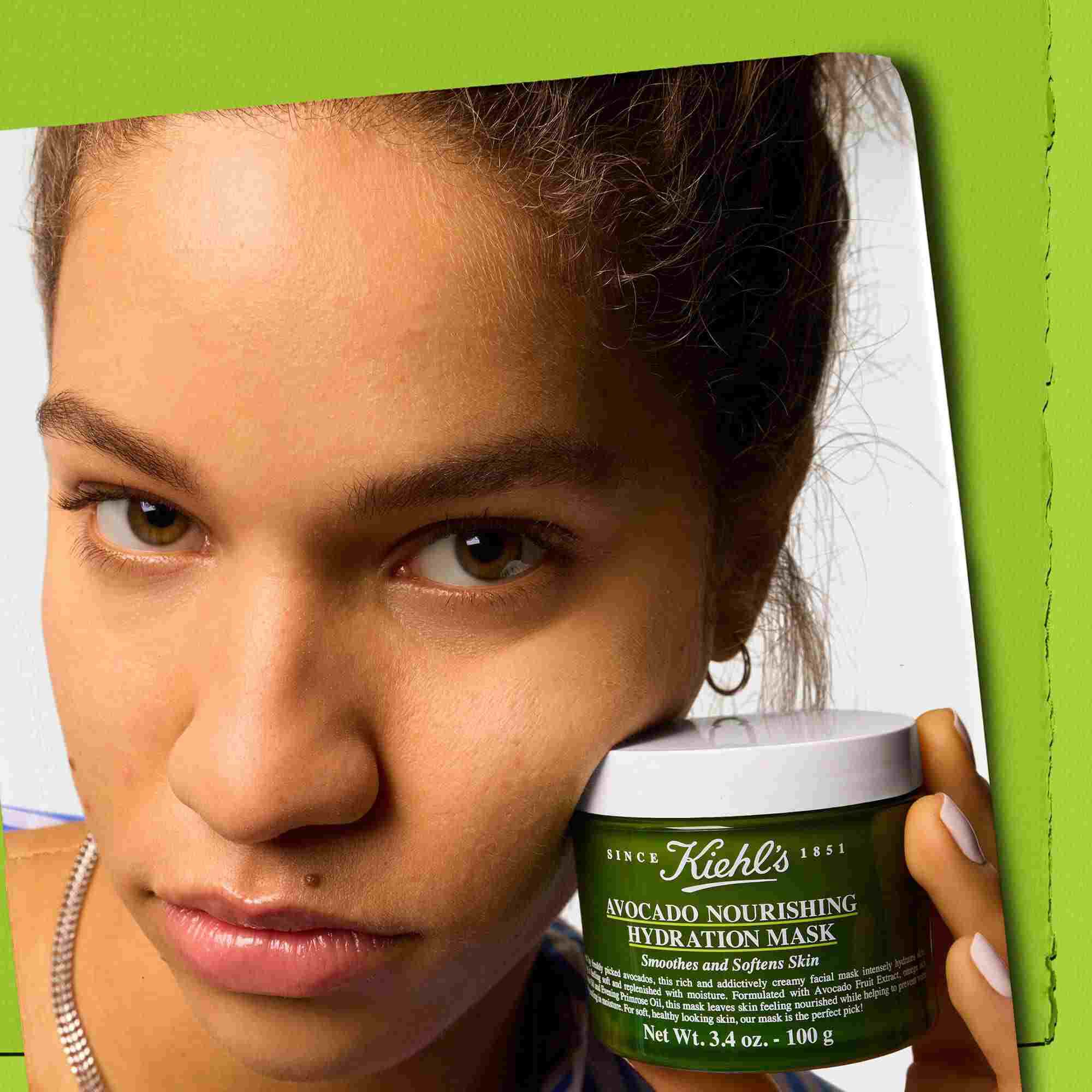 Model drži posudicu Kiehl's Avocado Nourishing Hydration Mask – zaglađuje i omekšava kožu
