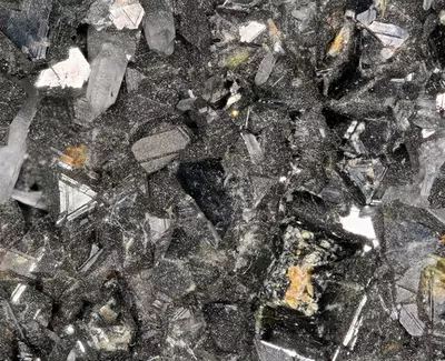 A close-up of shiny, crystal-like minerals with a dark, textured background, showcasing various shapes and reflections.