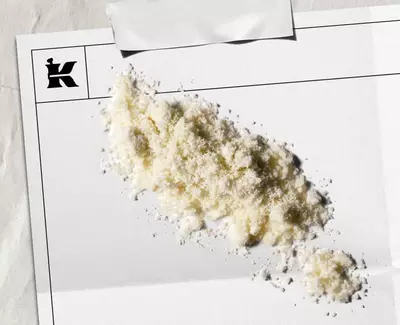 Prljavo-bijeli prah koji predstavlja 1% koloidne zobene pahuljice na bijeloj ploči s crnim Kiehl's logom u kutu.
