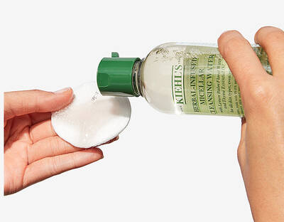 Osoba ulijeva Kiehl's biljni micelarni čistač na pamučni jastučić za njegu kože.