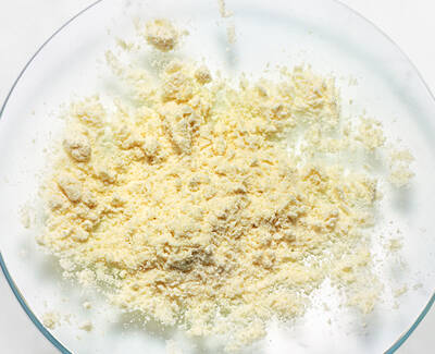 A clear glass dish containing a mound of light yellow, finely ground powder resting on a white background.