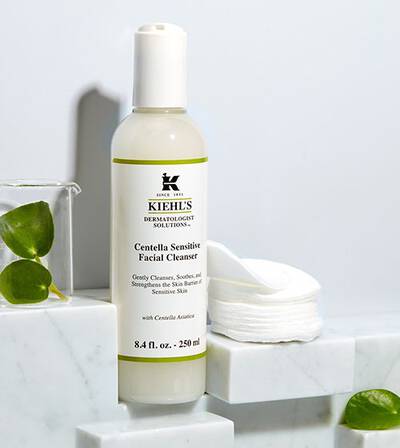 Bočica Kiehl's Centella Sensitive Facial Cleanser na mramornoj površini uz pamučne blazinice za njegu osjetljive kože.