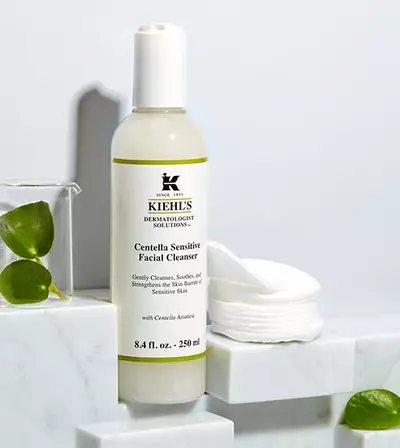 Bočica Kiehl's Centella Sensitive Facial Cleanser na mramornoj površini uz pamučne blazinice za njegu osjetljive kože.