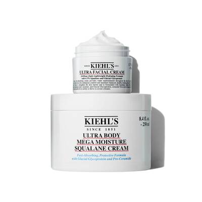 A container of Kiehl's Ultra Body Mega Moisture Squalane Cream and a smaller jar of Ultra Facial Cream, both featuring a clean, minimalist design with visible product labels.