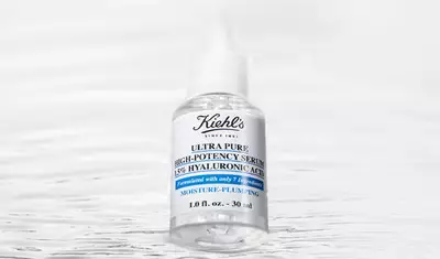 A clear glass bottle of Kiehl's Ultra Pure High-Potency Serum with a white label, featuring blue text and a dropper cap, set against a soft, blurred background.