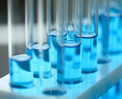 Close-up of test tubes filled with vibrant blue liquid, arranged in a white rack with soft lighting.