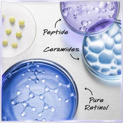 Alt text: A close-up of three petri dishes containing different skincare ingredients: one with a purple liquid labeled "Peptide," another with a blue gel labeled "Pure Retinol," and the third with a clear substance labeled "Ceramides." Small yellow spheres are arranged on a white surface beside the dishes.