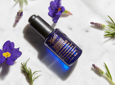 Bočica hidratantnog seruma s biljkom, okružena cvjetovima lavande i drugim biljem na mramornoj podlozi.