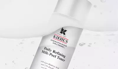 A bottle of Kiehl's Daily Refining Milk-Peel Toner, featuring a sleek design with white and silver colors, against a backdrop of flowing water.