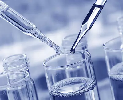A dropper is releasing liquid into a glass container, surrounded by other glass containers filled with liquid, in a laboratory setting.