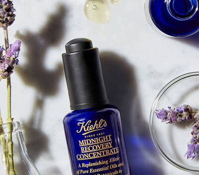 Plava bočica Kiehl's Midnight Recovery Concentrate okružena lavandom i uljima na mramornoj površini.